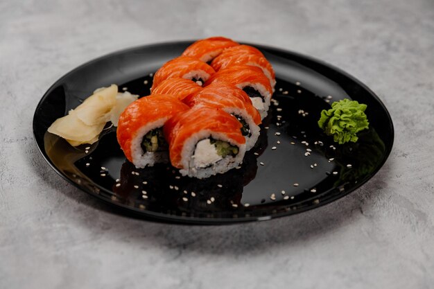 Huit portions de sushi saumon et concombre avec sauce vossabi et gingembre sur une assiette noire.