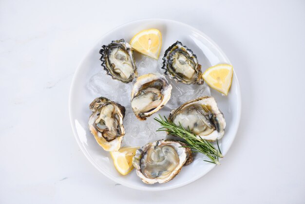 Huîtres fraîches de fruits de mer sur fond de plaque blanche - Coquille d'huître ouverte avec des épices aux herbes Romarin au citron servi sur table et glace Fruits de mer sains Dîner d'huîtres crues au restaurant Cuisine gastronomique