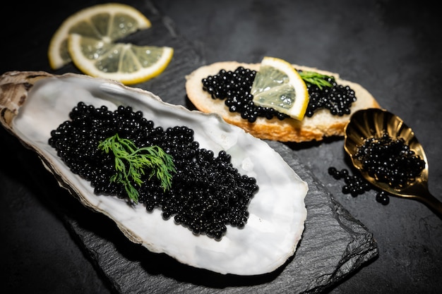 Photo huîtres ouvertes avec caviar d'esturgeon noir et citron sur glace sur table en béton noir. vue de dessus, mise à plat, espace de copie.