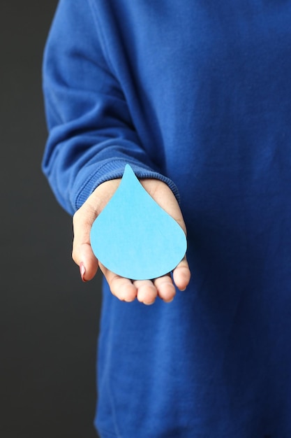 humain portant un pull bleu tenant une goutte d'eau en papier. Journée mondiale de l'eau, économisez l'eau.