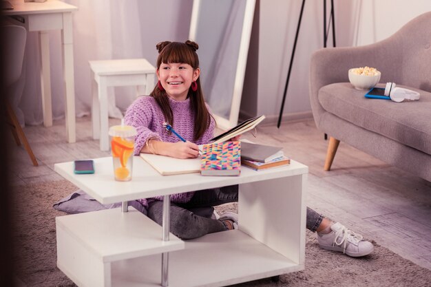 Humeur joyeuse. Adolescente heureuse gardant le sourire sur son visage tout en rêvant d'un excellent résultat