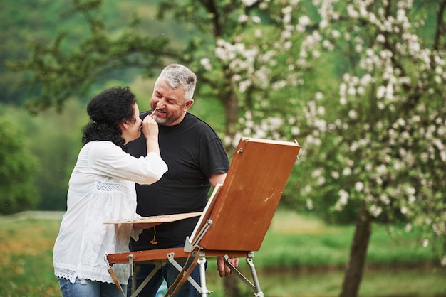 Humeur ludique. Couple d'âge mûr ont des journées de loisirs et travaillent ensemble sur la peinture dans le parc