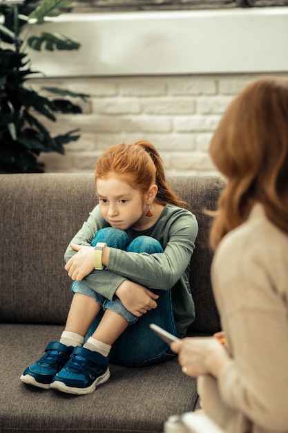 Humeur morose. Fille malheureuse sans gaieté mettant le menton sur ses genoux en pensant à ses problèmes