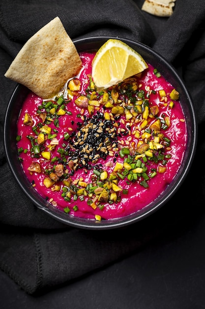 Hummus à la betterave et aux pois chiches maison avec crudités de légumes et pain sans levain sur fond sombre