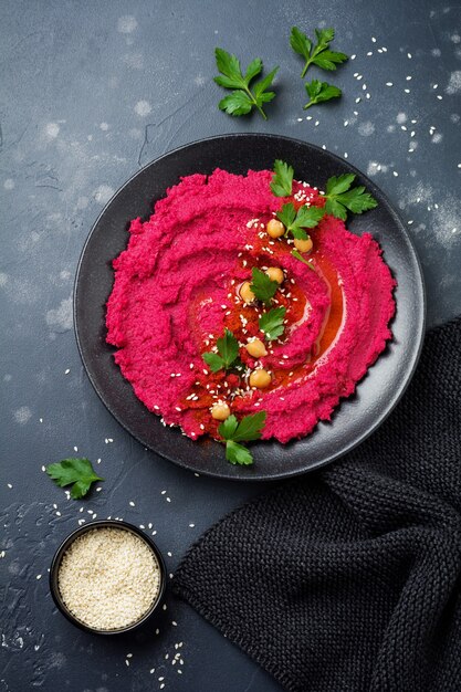 Hummus de betterave fait maison dans un plat en céramique noire sur fond de béton ancien