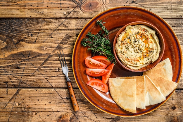 Hummus frais avec pain pita, tomate et persil sur une assiette rustique. fond en bois. Vue de dessus. Espace de copie.