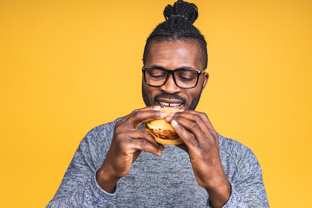 Hungry young african american man eating hamburger isolé sur fond jaune. Notion de régime.