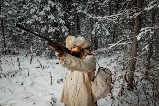 Hunter en vêtements vintage avec des armes à feu se faufile à travers la forêt