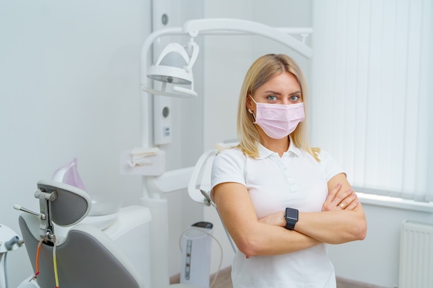 Hygiène buccale. Portrait de femme dentiste debout mains croisées sur fond de chaise de dentiste.