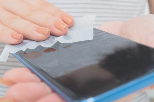 Hygiène pendant la pandémie de coronavirus Les mains des femmes essuient le smartphone avec une lingette antibactérienne