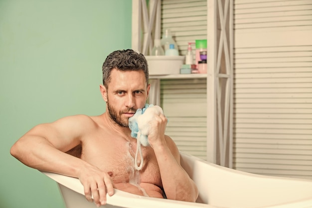 Hygiène et santé Sexualité et relaxation soins personnels Homme sexy dans la salle de bain désir et tentation Macho assis nu dans la baignoire se lavant avec une éponge homme laver le corps musclé avec une éponge en mousse