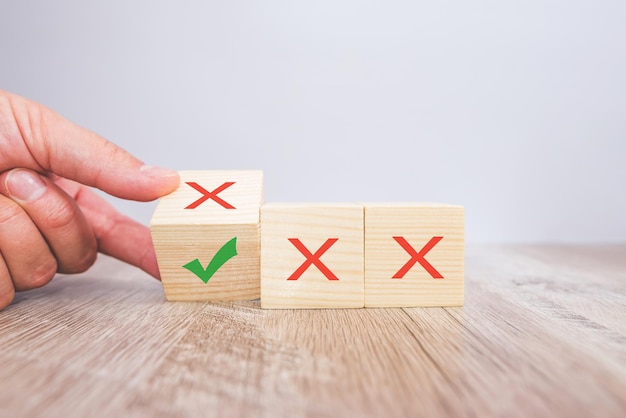 Icônes correctes et incorrectes sur des cubes en bois avec une main féminine choisissant la bonne icône sur le cube. Approbation, vote ou concept de décision correcte.