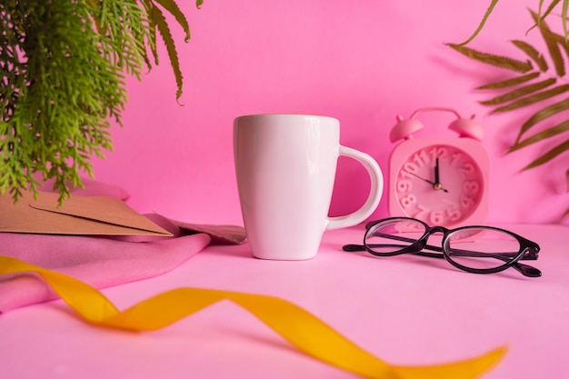 Idée de concept minimaliste tasse à café blanche sur fond rose avec décoration réveil, feuilles et verres