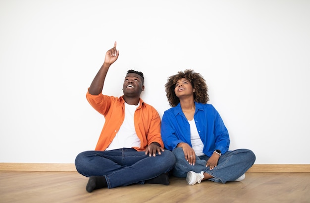 Idées de conception excité couple afro-américain pointant vers le haut assis sur le sol