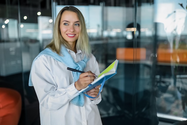 idées. Femme souriante blonde prenant des notes dans un cahier