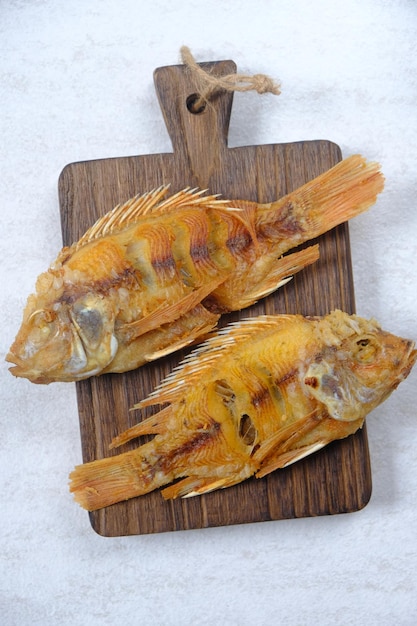 Ikan nila goreng. tilapia frit servi sur une planche à découper en bois de teck. protéines animales. Cuisine indonésienne