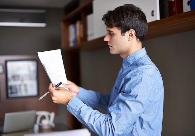 Il aspire à la perfection Photo d'un beau jeune homme d'affaires regardant par-dessus de la paperasse