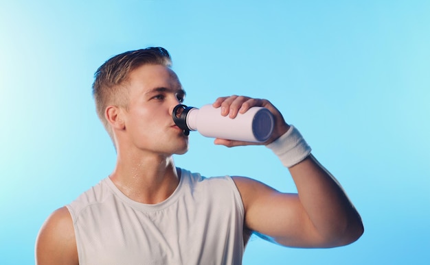 Il est important de rester hydraté Prise de vue en studio d'un beau jeune homme buvant dans une bouteille d'eau sur fond bleu