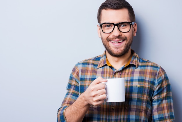 Il est temps d'avoir un frein. Beau jeune homme buvant du café et regardant la caméra en se tenant debout sur fond gris