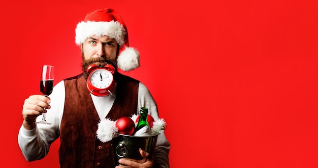 Il est temps de célébrer l'homme barbu en chapeau de Père Noël avec réveil le serveur tient un verre de vin et un seau