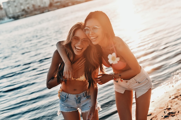 Il est temps de se détendre ! Deux jeunes femmes séduisantes en maillot de bain souriant tout en passant du temps insouciant sur la plage