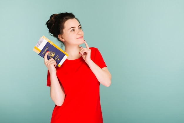 Il est temps de voyager. Une femme souriante à la mode moderne en robe rouge avec des billets d'avion et un passeport à la main.