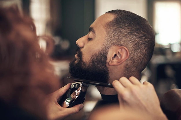 Il est très particulier à propos de sa barbe Photo d'un beau jeune homme assis et se faisant coiffer sa barbe par son coiffeur