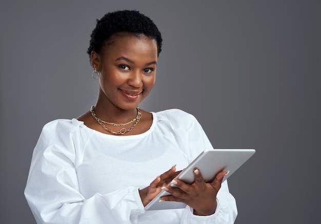 Il existe des tonnes de moyens rapides et faciles de gagner de l'argent en ligne Photo d'une jeune femme utilisant une tablette numérique debout sur un fond gris