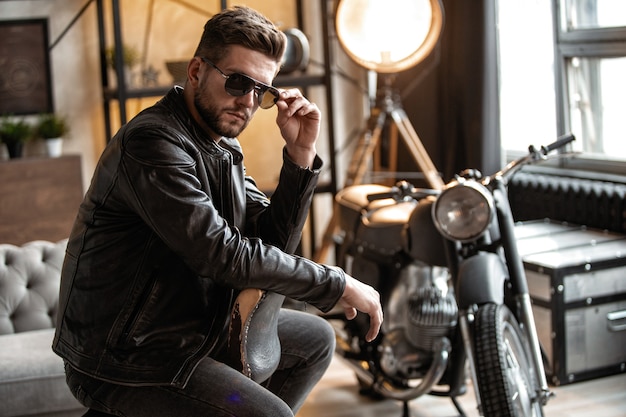 Il fera fondre votre cœur. Beau jeune homme en blouson de cuir à l'écart alors qu'il était assis sur le tabouret