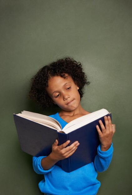 Il n'y a pas d'ami aussi fidèle qu'un livre Un jeune garçon ethnique lisant un livre debout devant un tableau noir