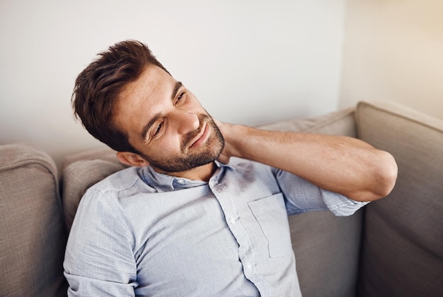 Il ressent un peu de tension sur son cou Photo d'un beau jeune homme tenant son cou de douleur tout en se relaxant sur un canapé à la maison