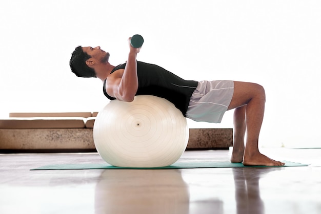 Il a trouvé un moyen de faire de l'exercice en position couchée Plan complet d'un homme soulevant des poids allongé sur un ballon d'exercice