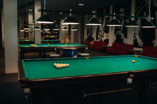 Il y a beaucoup de tables de billard avec des surfaces vertes et des boules dans le club de billard.
