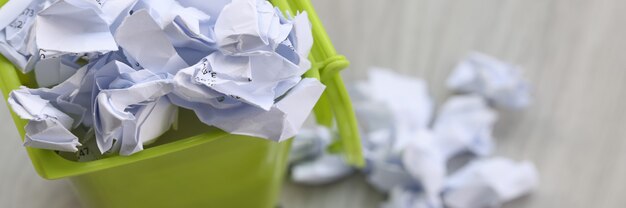 Il y a des morceaux de papier froissés dans une poubelle verte qui recycle le papier usagé