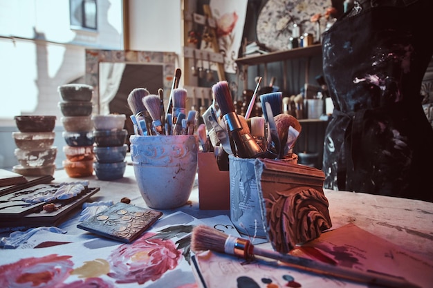 Il y a des pinceaux sombres et différents sur la table de l'artiste dans des bocaux. Il y a du gâchis d'artistick sur la table.