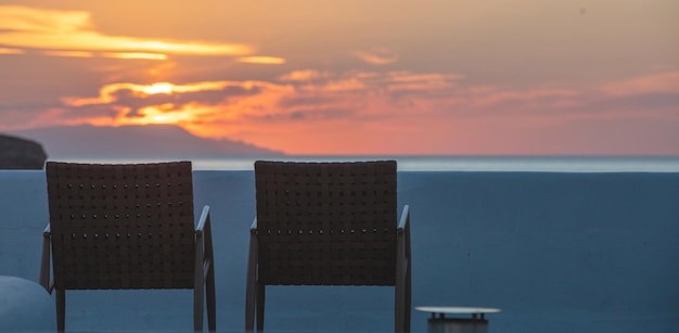 L'île des Cyclades en Grèce Deux chaise marron tissée vide en face de la mer Égée bleue au coucher du soleil
