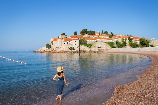 Île de Sveti Stefan, Monténégro 5 juillet 2021 : Mer Adriatique. Une fille au chapeau de paille se tient debout avec un verre de vin sur fond de l'île Saint-Étienne.
