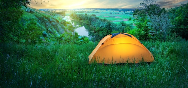 Photo illuminé de l'intérieur d'une tente orange sur une colline au-dessus de la rivière