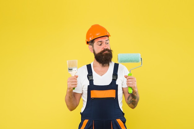 Illuminez chaque recoin et recoin. Fond jaune de travailleur de la construction. Le peintre tient le rouleau à peinture et le pinceau. Les travailleurs acharnés portent un chapeau de sécurité et un uniforme. Ouvrier qualifié. Peinture et décoration. Réparations.