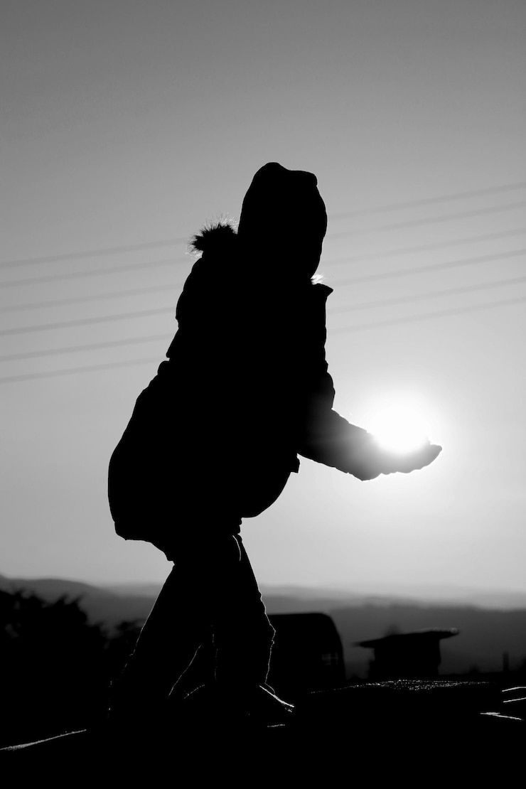 Photo illusion optique d'un garçon en silhouette tenant le soleil contre le ciel au coucher du soleil