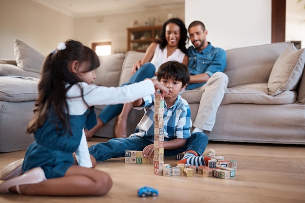 Ils jouent si bien ensemble Plan de deux jeunes frères et sœurs jouant avec leurs jouets pendant que leurs parents sont assis et regardent en arrière-plan