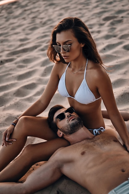 Ils ont trouvé l'amour. Beau jeune homme allongé sur sa belle petite amie tout en se relaxant sur la plage