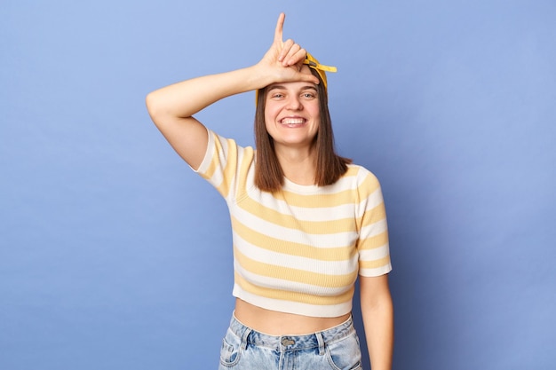 Image d'une adolescente joyeuse et joyeuse souriante portant un t-shirt rayé et une casquette de baseball posant isolé sur fond bleu regardant la caméra et montrant un geste plus lâche