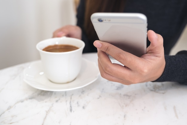 Image agrandi d&#39;une femme tenant et à l&#39;aide de smartphone tout en buvant du café au café