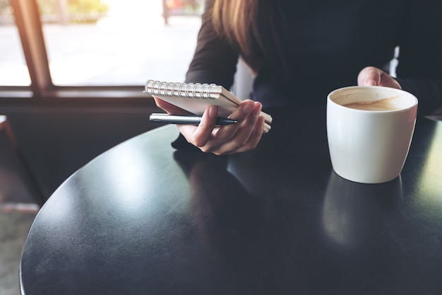 Image agrandi d&#39;une femme tenant un cahier blanc vierge et une tasse de café sur la table