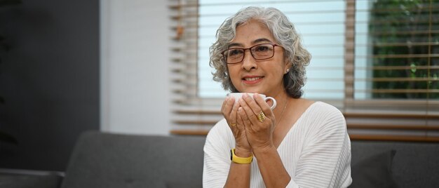 Image d'une agréable femme d'âge moyen se relaxant sur le canapé et appréciant son café du matin Concept de style de vie réessayé