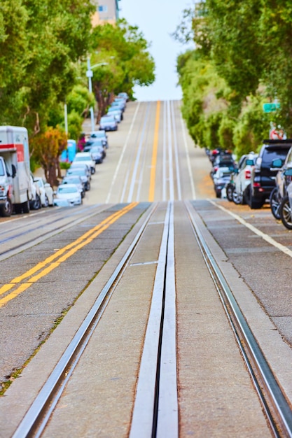 Image d'un angle faible sur des voies métalliques de tramway sur une route avec une colline floue en arrière-plan bordée d'arbres