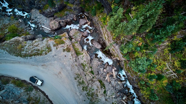 Image de l'antenne regardant le chemin de terre avec une jeep blanche près des falaises avec les rapides de la rivière ci-dessous