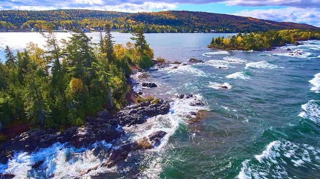 Image d'antenne de vagues et d'une forêt d'automne avec des arbres verts, rouges, jaunes et oranges et une île d'arbres