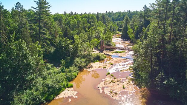 Image de l'antenne vers le bas de la grande rivière brune dans la forêt verte avec pont suspendu et deux randonneurs